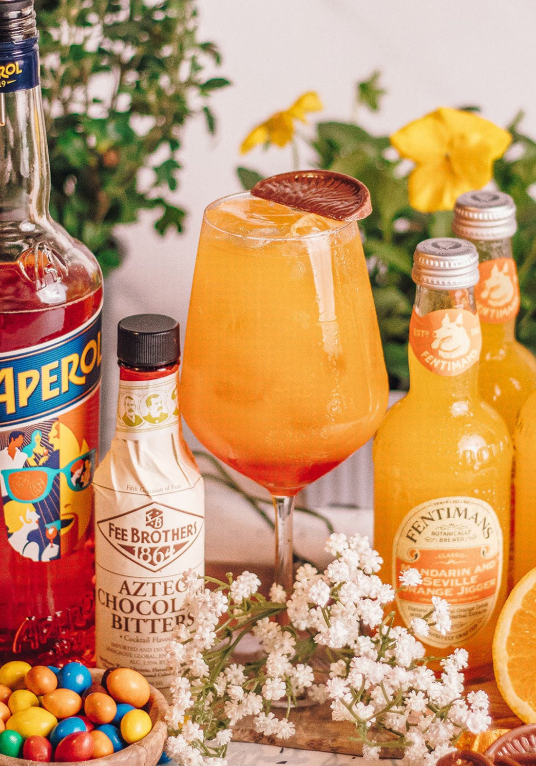An orange serve topped with a segment of chocolate orange beside a bottle of Aperol and Fentimans Mandarin & Seville Orange Jigger with some chocolate eggs and florals on the table