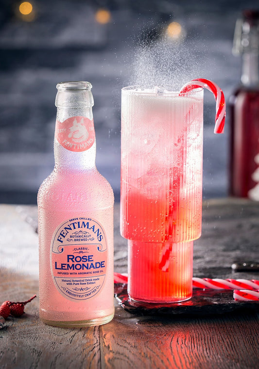 A bottle of Fentimans Rose Lemonade with a highball serve garnished with a red and white candy cane