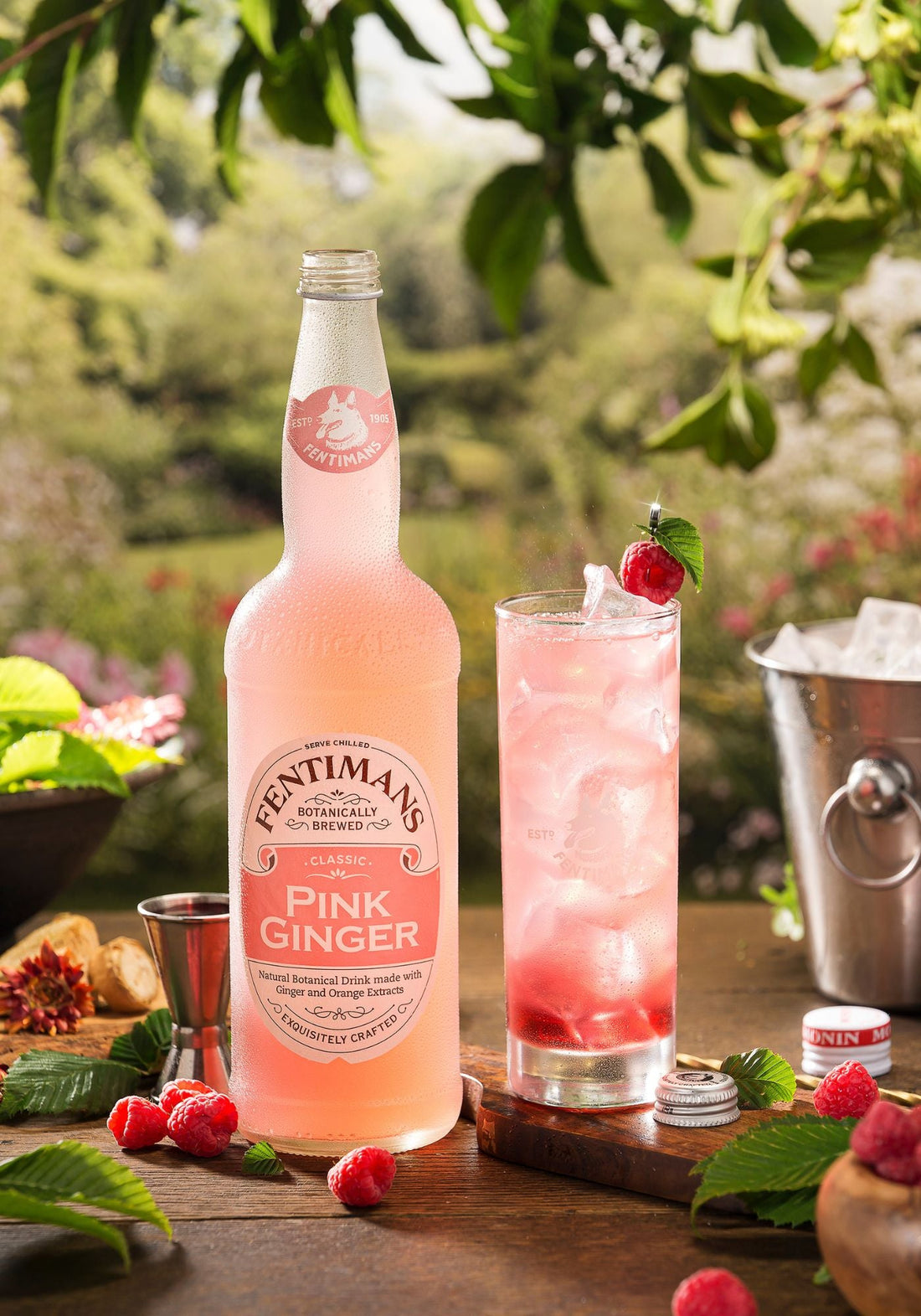 The Fearless cocktail in a highball glass beside a bottle of Fentimans Pink Ginger in a garden setting